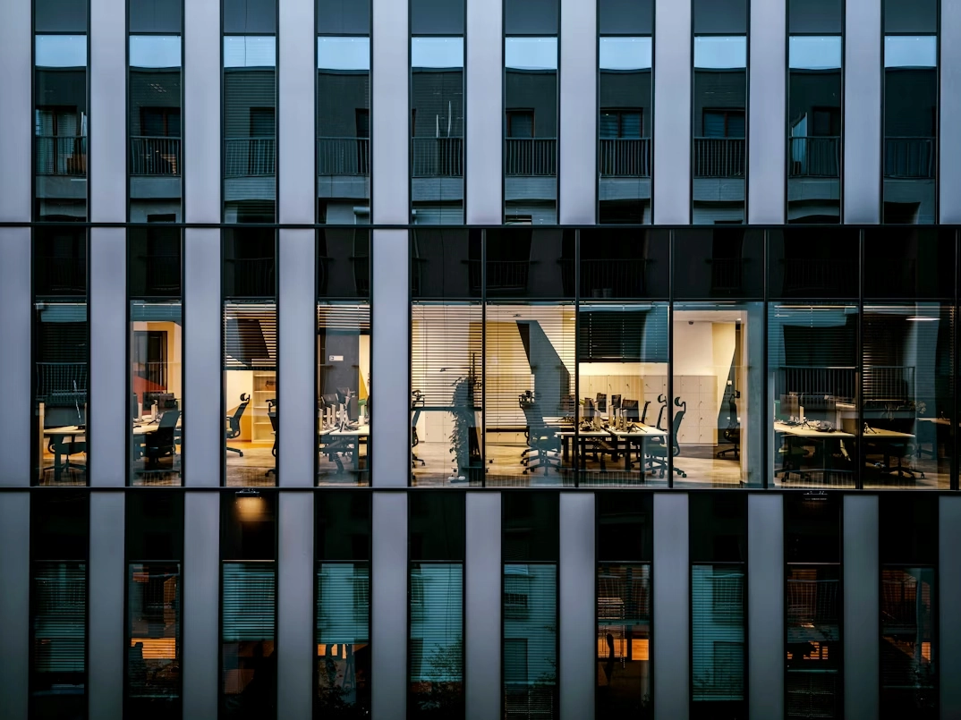 Diseño de oficinas sostenibles: cómo crear espacios eficientes Vista de oficina desde fuera de un edificio a través de la cristalera